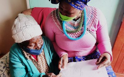 MEC Nonceba Kontsiwe showing an old lady how to sign a title deed during a house visit in Burgersdorp to handover tittle deeds.