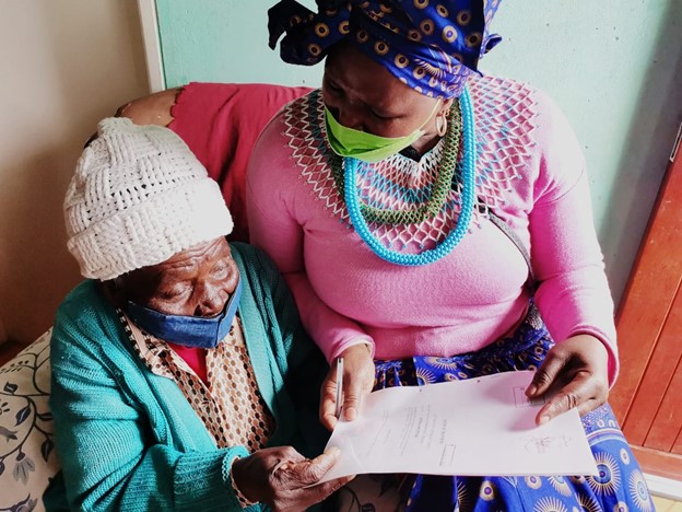 MEC Nonceba Kontsiwe showing an old lady how to sign a title deed during a house visit in Burgersdorp to handover tittle deeds.